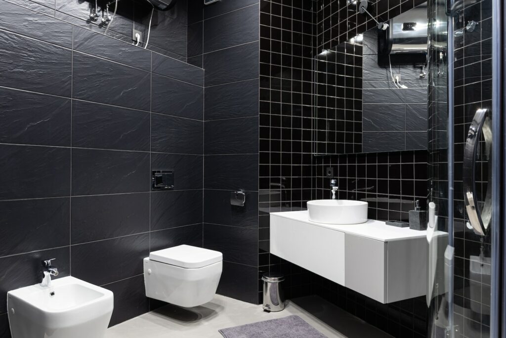 Interior design of modern bathroom with sink and bidet with mirror and decorated with black tile